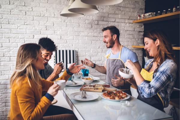 A group of happy housemates are eating a meal together. Following these tips for housemates will allow for a great living experience. 