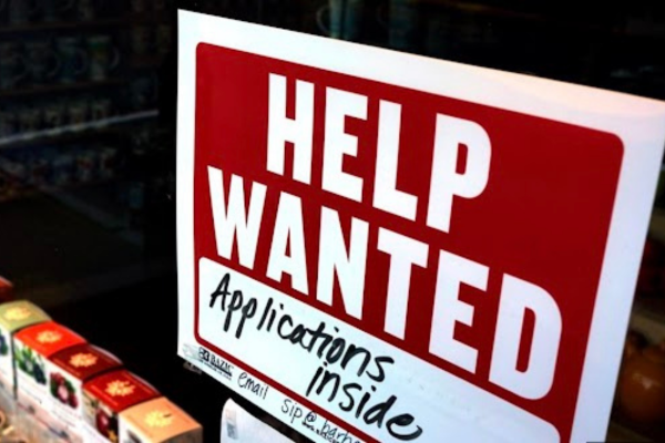 A red and white sign appears in a window with text that reads Help Wanted Applications Inside. Discover more about Canada's most recent job report. 