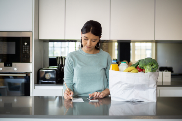 A young woman is reviewing her budget after grocery shopping. Inflation in Canada can affect monthly expenses and the cost of living. 