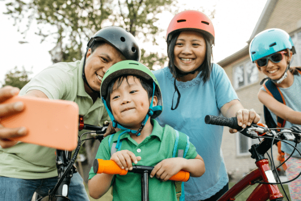 A family of four taking a selfie on their bikes and wearing helmets. The Alberta health card covers basic medical services you may need in case of medical emergencies.