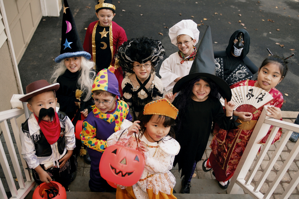 Children dressed in happy Halloween costumes waiting to receive candy at the front door of a neighbourhood home.