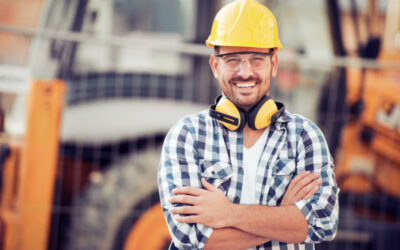Construction worker smiling and crossing arms in front of vehicle on site