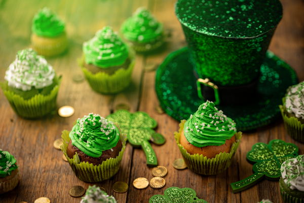 Festive cupcakes iced with green frosting, shamrocks, and a leprechaun hat. St. Patrick's day food can include corned beef and cabbage, or colcannon.