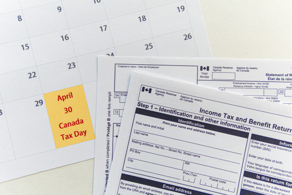 A paper copy of a Canadian Income Tax Return is placed on top of a calendar showing the tax deadline. 
