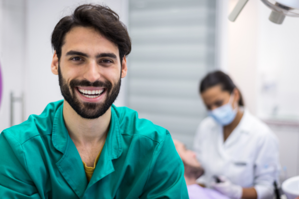 Close up picture of a male dentist with a dental hygienist and patient in the background