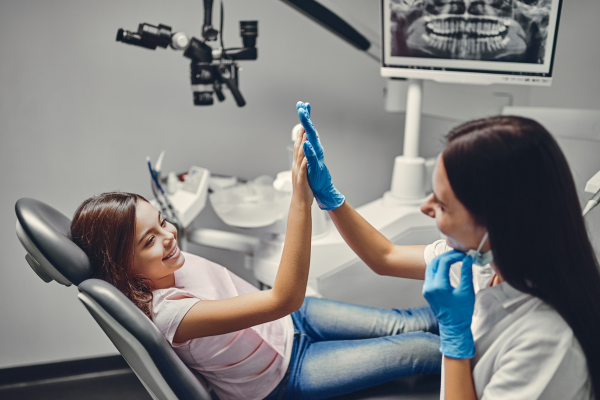 A female dentist is giving good news to a young patient sitting in a dental chair after a successful exam.