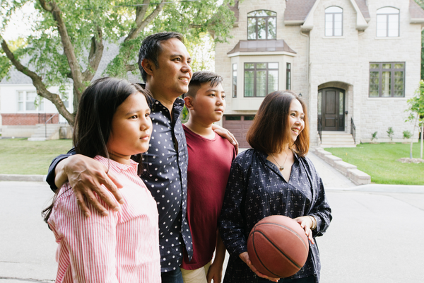 Newcomer family with two teens standing in front of residential homes while searching for accommodation in Canada.