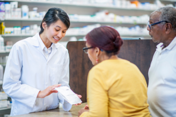 Female pharmacist giving medication advice to an elderly couple in a store pharmacy.