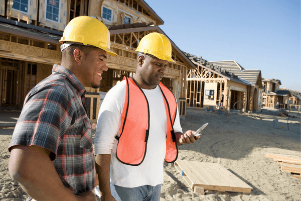 Two construction workers using a mobile phone at a residential constructions site. 