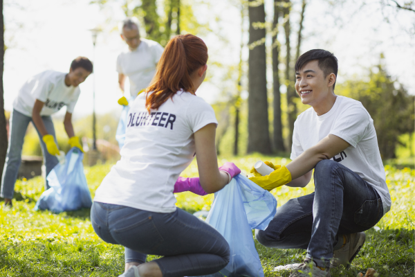 A group of happy volunteers are picking in litter in a park. A common Earth Day activity is volunteering in community clean-up events.