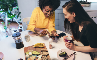 Two young women sharing accommodation are having breakfast together and looking at a smartphone.