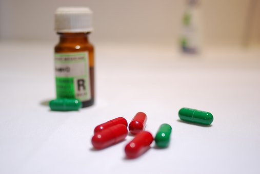 Medication bottle with a prescription label on it along with several capsules beside the bottle. 