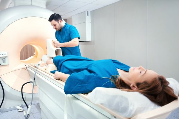 Medical radiation technologist operating a CT scanner with a female patient.