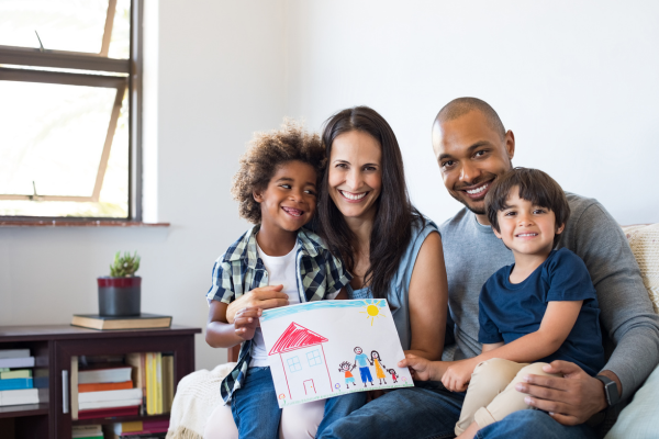 A mixed-race couple is sitting in their new home in Canada with their two young children. Settlement services in Canada can give newcomers an advantage before and after arriving. 