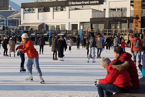 People enjoying a bright sunny day at an outdoor skating rink during the winter season in Canada.